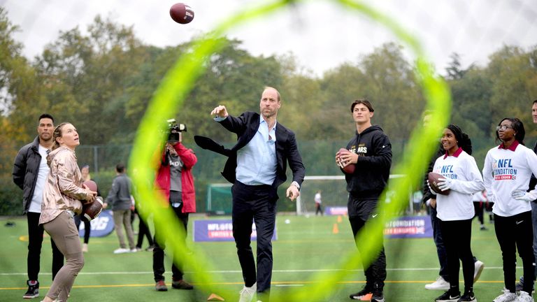 Princ z Walesu hází fotbalem na cíl, sleduje ho Louis Rees-Zammit, vlevo, když se účastní akce NFL Foundation Flag.