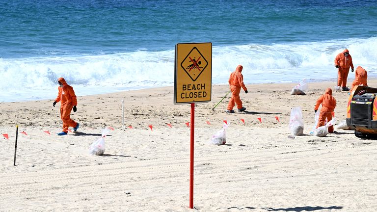 Pracovníci v ochranných oděvech uklízejí neznámé trosky vyplavené na pláži Coogee v Sydney v Austrálii.  Obr: AAP/Reutrers