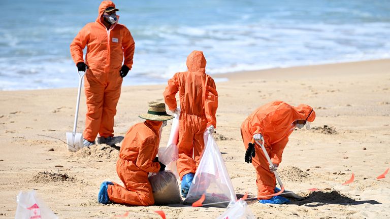 Pracovníci v ochranných oděvech uklízejí neznámé trosky vyplavené na Coogee Beach.  Obr: AAP/Reuters