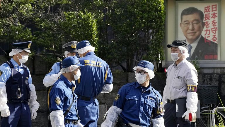 Policisté poblíž sídla Liberálně demokratické strany Japonska s plakátem japonského premiéra Shigeru Ishiby. Obrázek: AP