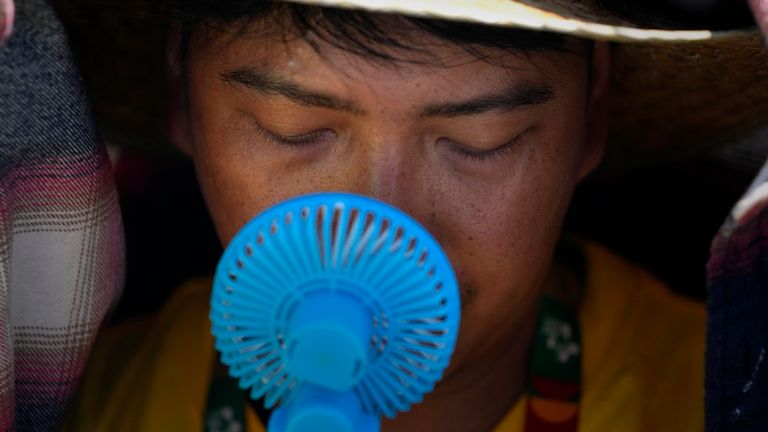 SOUBOR - Dobrovolník Světových dnů mládeže používá malý ventilátor, aby se ochladil z intenzivního horka, když čeká před příjezdem papeže Františka na Passeio Mar.timo v Alg..s, kousek od Lisabonu, 6. srpna 2023. Evropská agentura pro klima vypočítává, že listopad šestý měsíc v řadě stanovila zeměkoule nový měsíční rekord v horku a přidala k překonaným rekordům letošního tepla nejteplejší podzim. (AP Photo/Armando Franca, soubor)