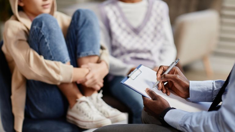 Detailní záběr afroamerického psychologa zapisování poznámek do schránky v terapeutické relaci pro děti. Obrázek: iStock