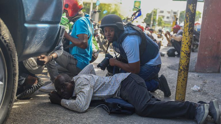 Novináři se kryjí před střelbou mezi gangy a policií v Port-au-Prince na Haiti, pondělí 11. listopadu 2024. (AP Photo/Odelyn Joseph)