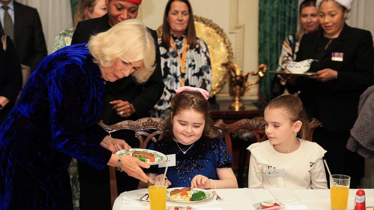 Královna Camilla drží talíř s jídlem, když se v Clarence House v Londýně setkává s rodiči a dětmi podporovanými Helen & Douglas House a Roald Dahl's Marvelous Children's Charity. Datum snímku: čtvrtek 12. prosince 2024. Mina Kim/PA Wire