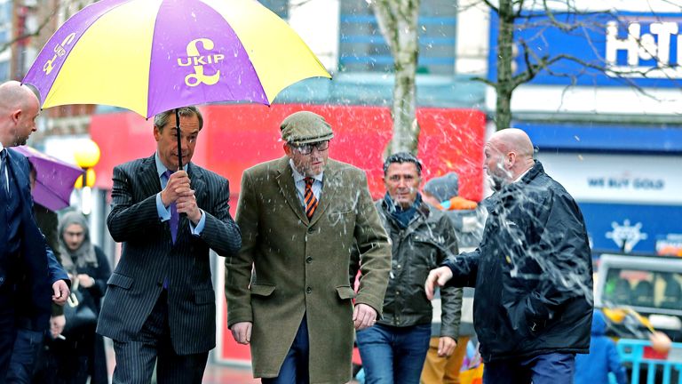 Mladík (není na obrázku) hází vejce na bývalého vůdce Ukip Nigela Farage (uprostřed vlevo), když vítá vůdce Ukip Paula Nuttalla (uprostřed vpravo) poblíž kanceláře Paulovy kampaně ve Stoke-on-Trent, Staffordshire.