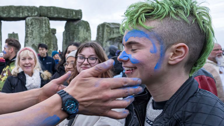 Obličej člověka je potřený modrou barvou, když se účastní oslav zimního slunovratu ve Stonehenge, Anglie, v sobotu 21. prosince 2024. (AP Photo/Anthony Upton)