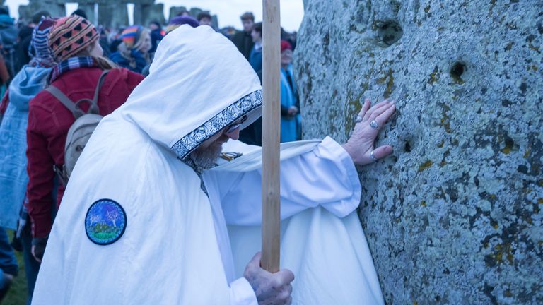 Muž položí ruce na jeden z kamenů během oslav zimního slunovratu ve Stonehenge, Anglie, sobota 21. prosince 2024. (AP Photo/Anthony Upton)