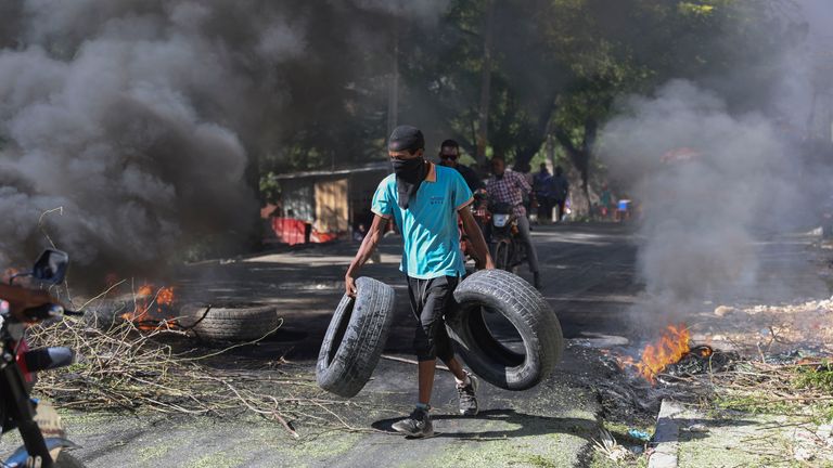 Rezident nese pneumatiky, které mají být přidány na hořící barikádu, aby odradily členy gangu od vstupu do jeho čtvrti, v Port-au-Prince, Haiti, úterý 19. listopadu 2024. (AP Photo/Odelyn Joseph)