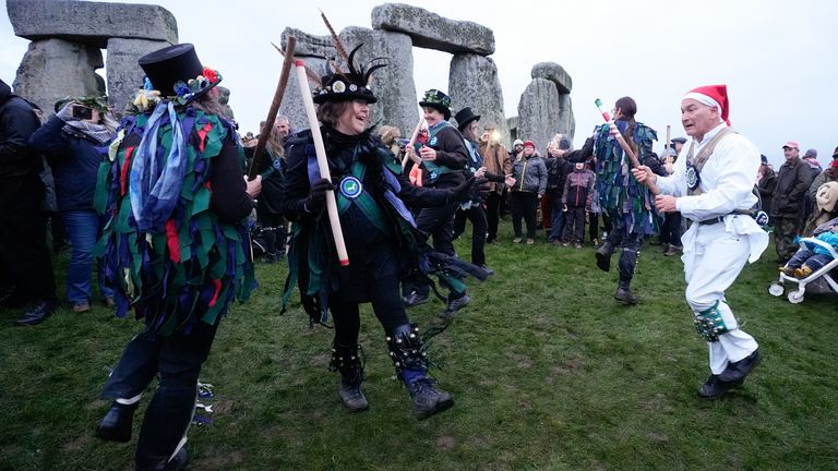 Tanečníci Morris vystupují před kameny, když se lidé účastní oslav zimního slunovratu během východu slunce u prehistorického monumentu Stonehenge na Salisbury Plain ve Wiltshire. Datum snímku: Sobota 21. prosince 2024.