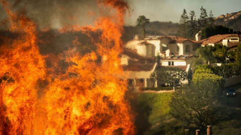 Plameny stoupají, jak požár Palisades postupuje na domy v sousedství Pacific Palisades v Los Angeles, úterý 7. ledna 2025. (AP Photo/Ethan Swope)