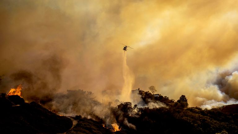 Voda je svržena na postupující požár Palisades vrtulníkem v sousedství Pacific Palisades v Los Angeles, úterý 7. ledna 2025. (AP Photo/Ethan Swope)