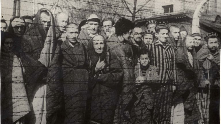 Přeživší holocaustu stojí za plotem z ostnatého drátu po osvobození nacistického německého vyhlazovacího tábora Auschwitz-Birkenau v roce 1945. Obr: Yad Vashem Archives/Handout via Reuters