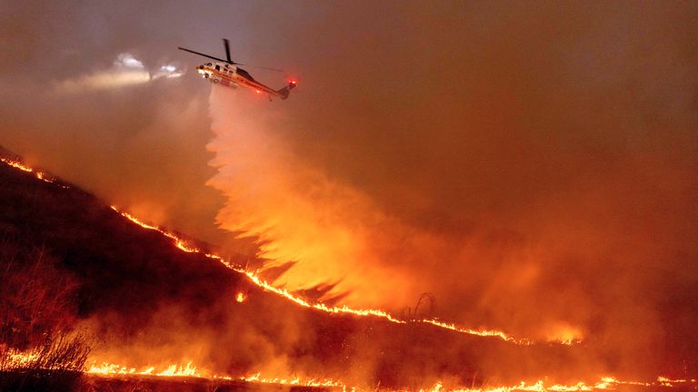 Voda je shozena vrtulníkem na Kenneth Fire v části West Hills v Los Angeles, čtvrtek 9. ledna 2025. (AP Photo/Ethan Swope)