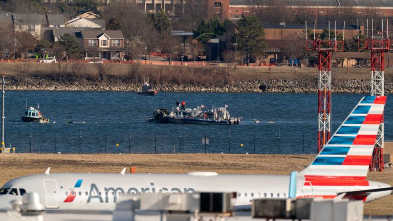 Policejní a pobřežní strážní lodě jsou vidět kolem trosky v řece Potomac, protože letadlo American Airlines prochází v popředí na národním letišti Ronald Reagan Washington, sobota 1. února 2025, v Arlingtonu, Va., (AP Photo/Jose Luis Magana)