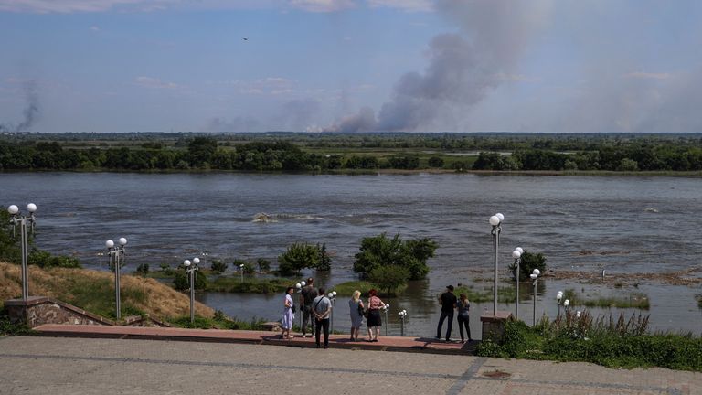 Místní obyvatelé stojí na nábřeží řeky Dnipro, která zaplavila po přehradě Nova Kakhorka, která byla porušena, když se kouř stoupal po ostřelování na protějším břehu, uprostřed ruského útoku na Ukrajinu, v Khersonu, ukrajinu 6. června 2023. Reuters/Ivan Antypenko