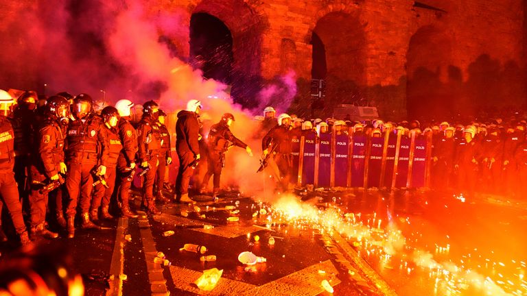 Policejní důstojník kopne světlice hozenou protestujícími během střetů na shromáždění proti zatčení starosty Istanbulu Ekrem Imamoglu, v Istanbulu, Turecko, pátek 21. března 2025. (AP Photo/Khalil Hamra)