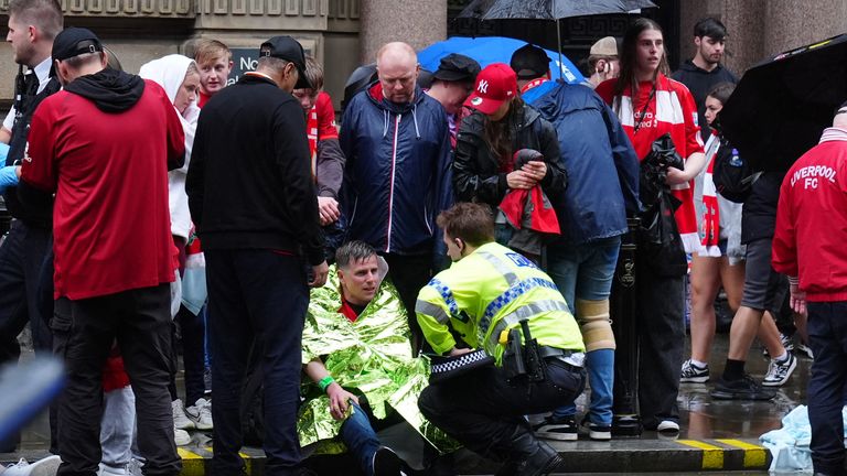 Postávka Liverpoolu sedí na zemi obklopené jinými fanoušky. Pic: Pa