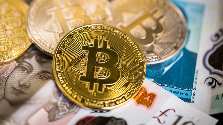 Londýn, Velká Británie - 23. ledna 2018: Obrázek zblízka barevný obrázek zobrazující sbírku lesklých zlatých a stříbrných bitcoinů, fyzický projev digitální virtuální kryptoměny. Bitcoiny odpočívají na vrcholu hromady bankovních bank British Pound Bank, včetně poznámky 5 £, 10 GBP a 20 GBP. Spousta prostoru pro kopírovací prostor.