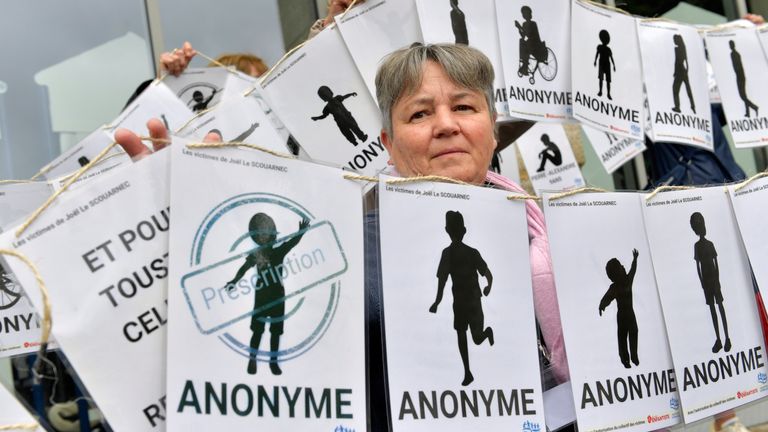 Žena zaznamenává za bannerem představujícím anonymní oběti během demonstrace před rozsudkem v soudním řízení s Joel Le Scouarnec, 74letým bývalým chirurgem, obviněný z znásilnění a sexuálního napadení 299 dětí, středa 28. května 2025 ve Vannes, Brittany v západní Francii. (AP Photo/Mathieu Pattier)