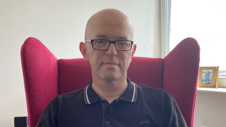   Chris Penfold-Ivany, holohlavý bílý muž středního věku s černým pólo a brýle seděl na židli, který mluvil s Sky News