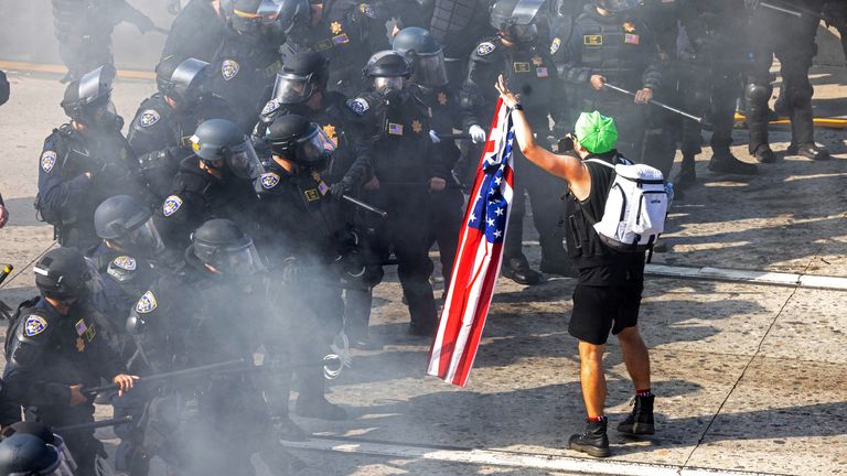 Demonstrátor drží americkou vlajku naproti důstojníkům dálniční hlídky California (CHP) během protestu proti federálním imigračním zametáním, v 