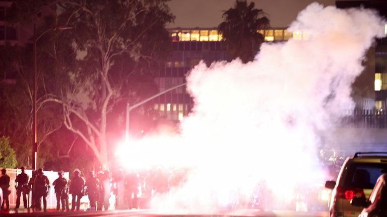 Policisté se staví stráž, protože kouř pokrývá oblast během protestu proti federálním imigračním zametáním v centru Los Angeles v Kalifornii