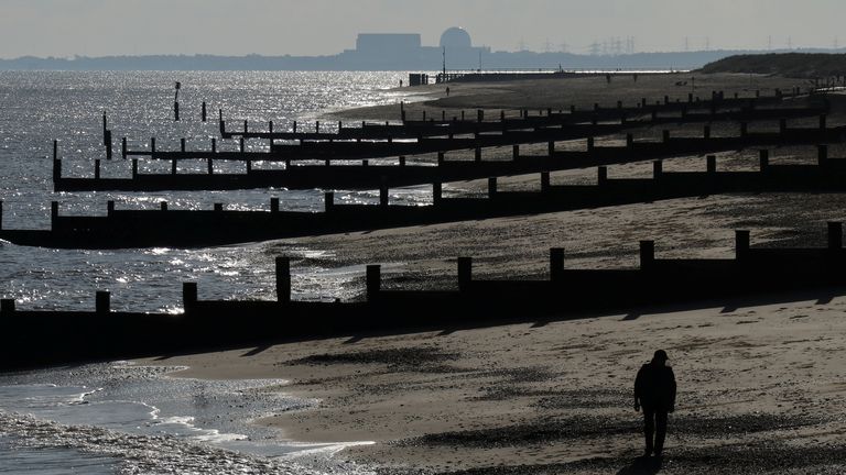 Muž chodí podél pobřeží Suffolku s jadernou elektrárnou Sizewell B na obzoru
