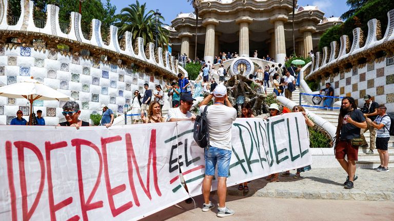 Turista odmítá přesunout pro demonstranty, kteří drží banner, který čte, který čte "Obnovte Park Guell" v Barceloně. Pic: Reuters