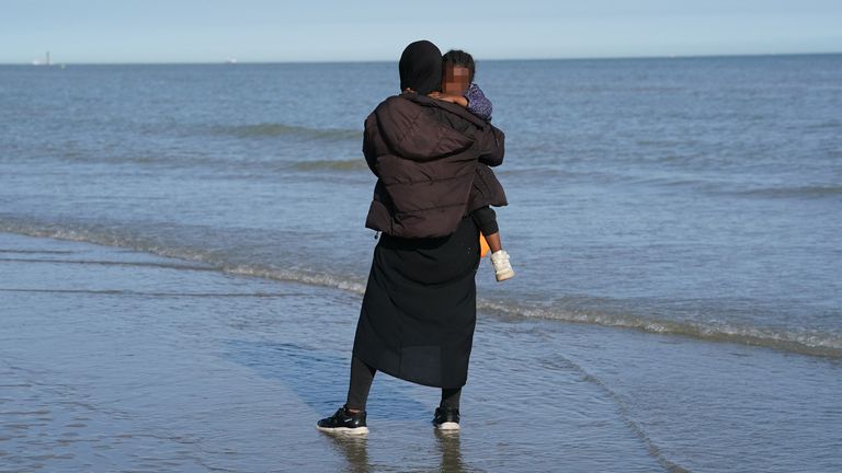 Mezi skupinou lidí je vidět malé dítě, které se domnívají, že jsou migranti a čekají na pláži ve Francii Gravelines