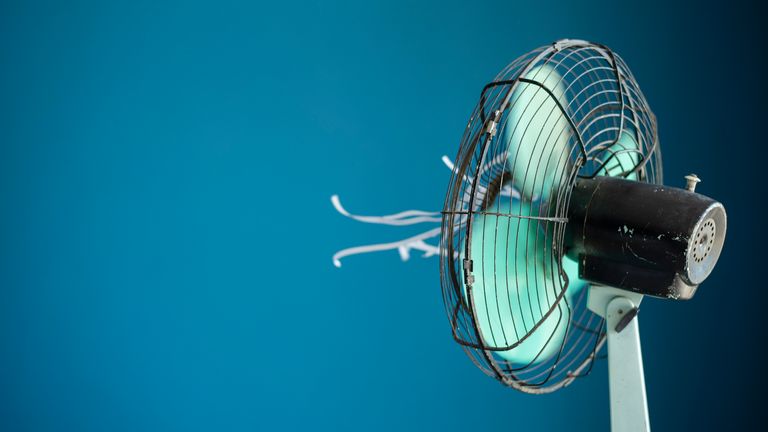 Snímek kovového elektrického ventilátoru s bílými streamery připevněnými na modrém pozadí