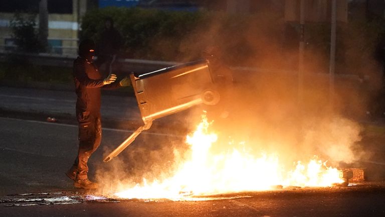 Protestující hodí koš do ohně hořící na ulici. Pic: Pa