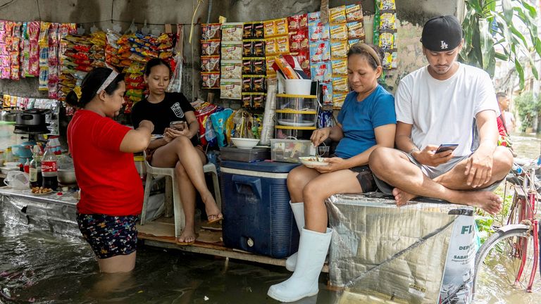 Lidé odpočívají v dalším obchodě podél zatopené ulice po těžkých deštích, které přinesl Typhoon Co-May v Navotas City, Metro Manila, Filipíny, 25. července 2025. Reuters/Lisa Marie David