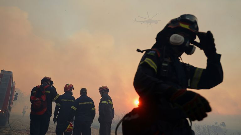 Hasiči se snaží uhasit plameny jako vrtulníku letící během požáru, na severozápadním předměstí Kryoneri, v Aténách v Řecku, sobota 26. července 2025. (AP Photo/Yorgos Karahalis)