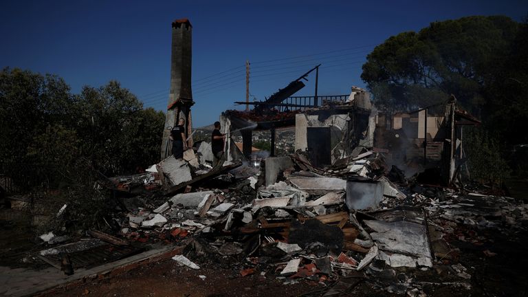 Dobrovolný hasič používá hadici k ochlazení spáleného domu během požáru ve městě Koropi poblíž Athén. Pic: Reuters