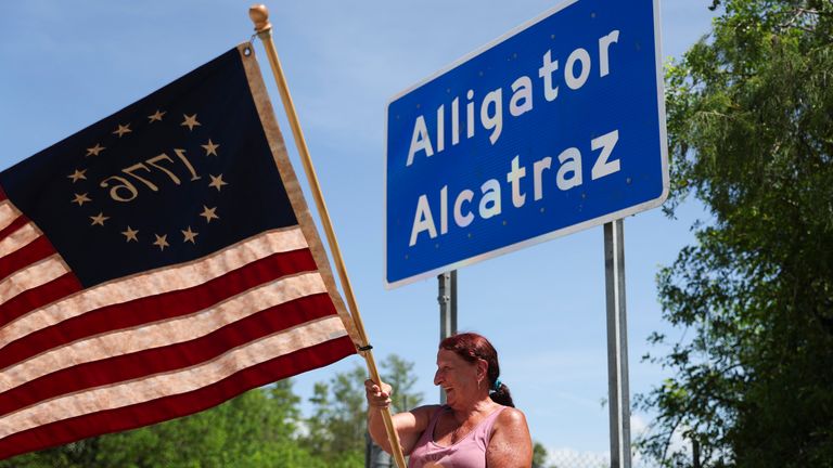 Rana Mourer mává americkou vlajku mimo detenční zařízení migrujícího dabovanou "Aligátor Alcatraz," V tréninkovém a přechodovém zařízení Dade-Collier, sobota 12. července 2025 v Ochopee, Florida (AP Photo/Alexandra Rodriguez)