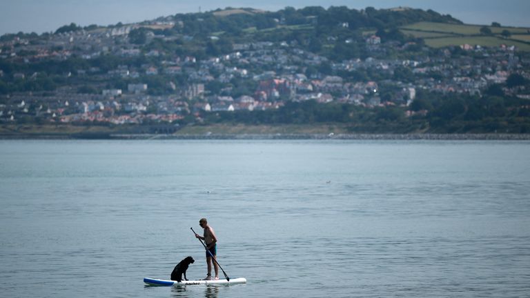 Muž stojí na paddleboardu se svým psem poblíž pláže na Rhos-on-Sea ve Walesu. Pic: Reuters