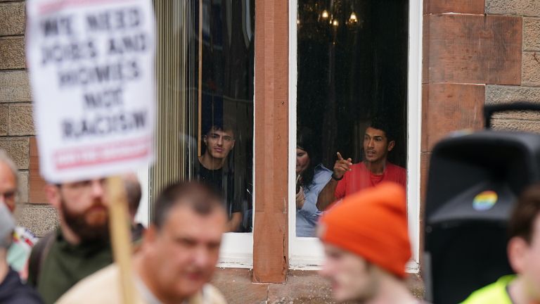 Lidé uvnitř hotelu se dívají na protestující před hotelem Radisson v Perthu. Pic: Pa